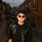 A stylish young man wearing sunglasses and a leather jacket on a colorful urban street.